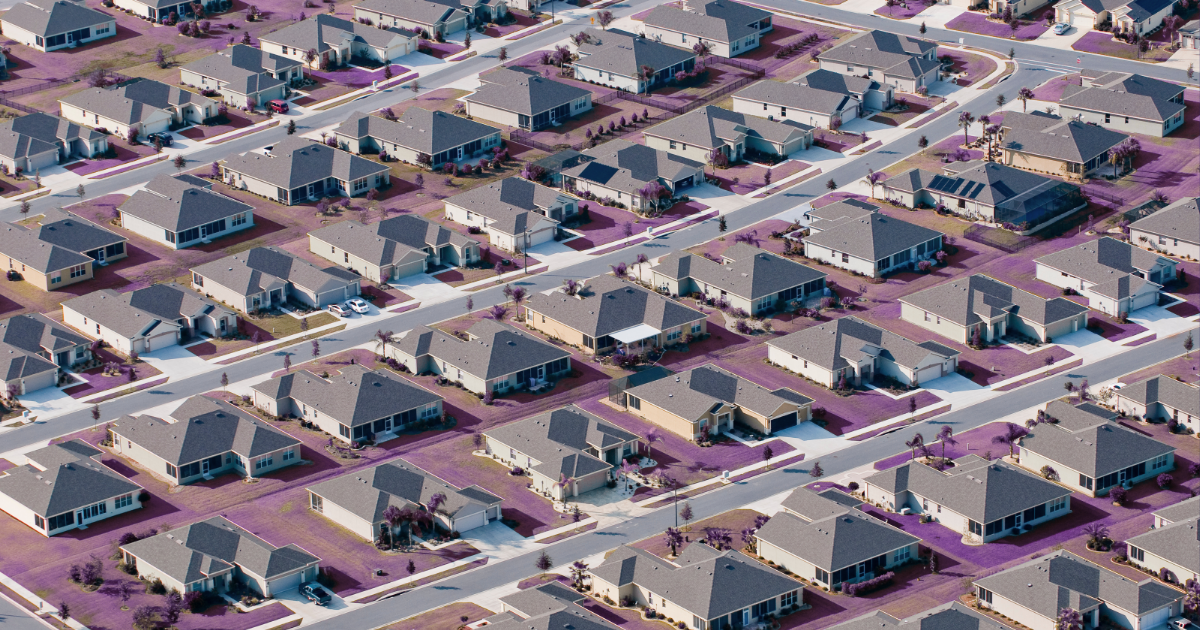 Aerial view of a suburban neighborhood with identical single-story houses, gray roofs, and yards. For real estate article.