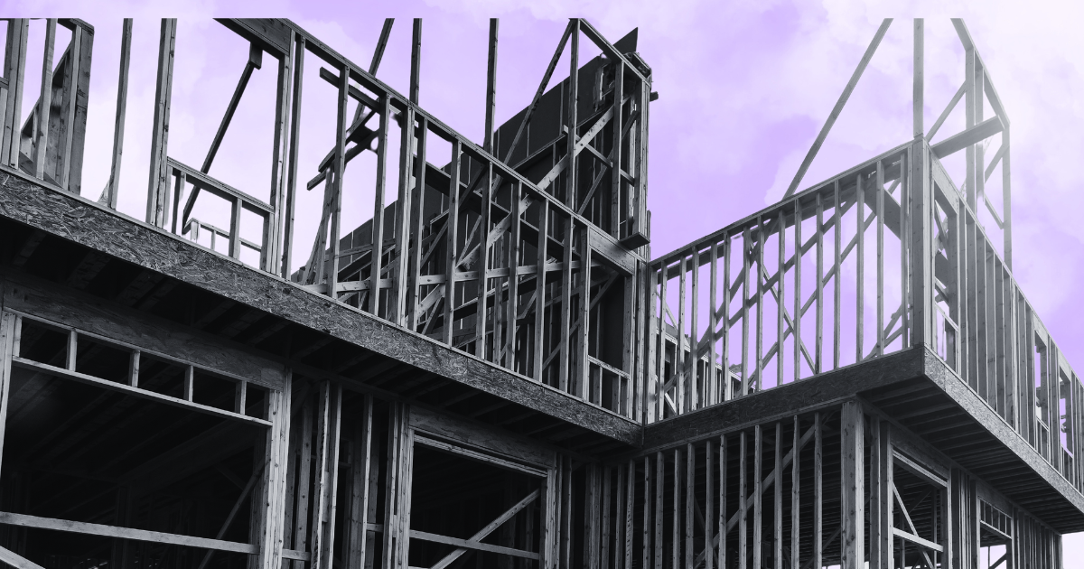 Black and white image of a house under construction with exposed beams against a purple sky, for a real estate article.