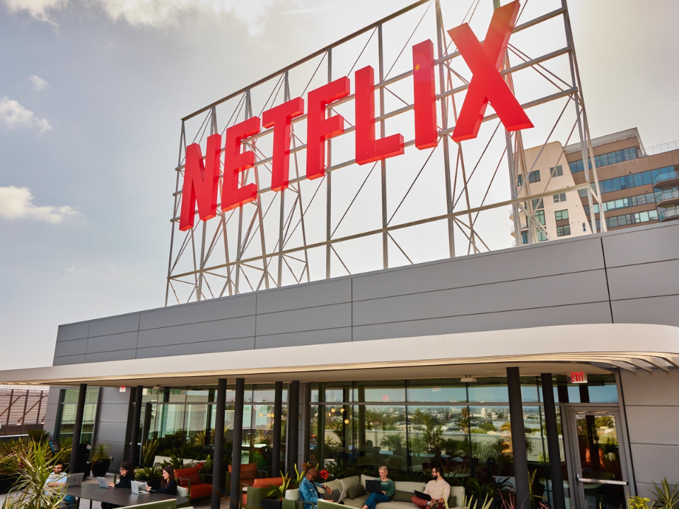 Netflix sign on a modern building with rooftop seating. Clear sky and another building in the background. For real estate article.