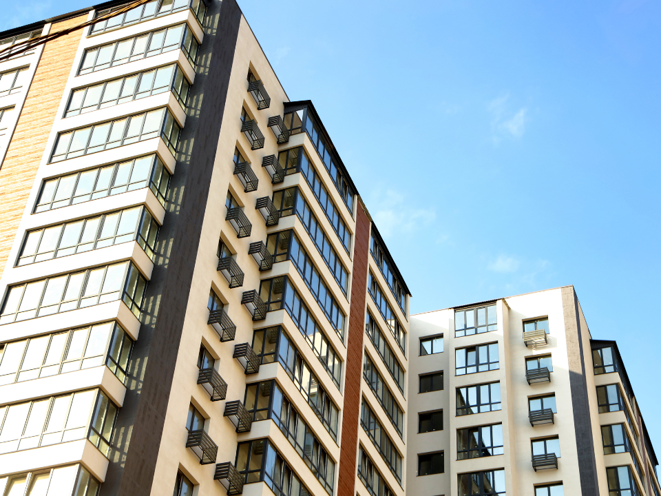 Two modern apartment buildings with large windows and balconies against a clear blue sky, featured in a real estate article.