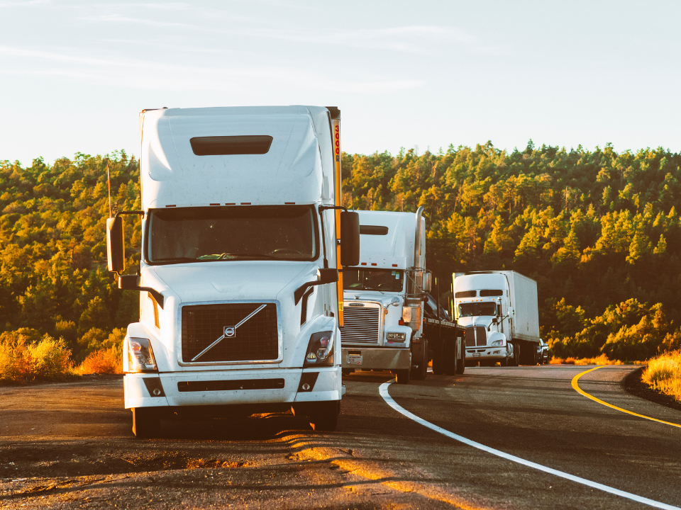 Three white trucks parked on a winding road with green trees; image for real estate article about US Logistics Solutions bankruptcy.