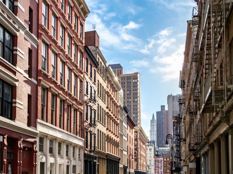 City street with classic and modern buildings, fire escapes visible, skyscrapers in background; for NYC Section 8 article.