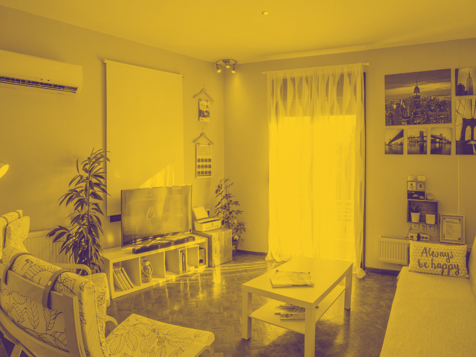 Cozy living room with TV, plants, light couch, and coffee table on wooden floor. Warm lighting and wall art. For real estate site.