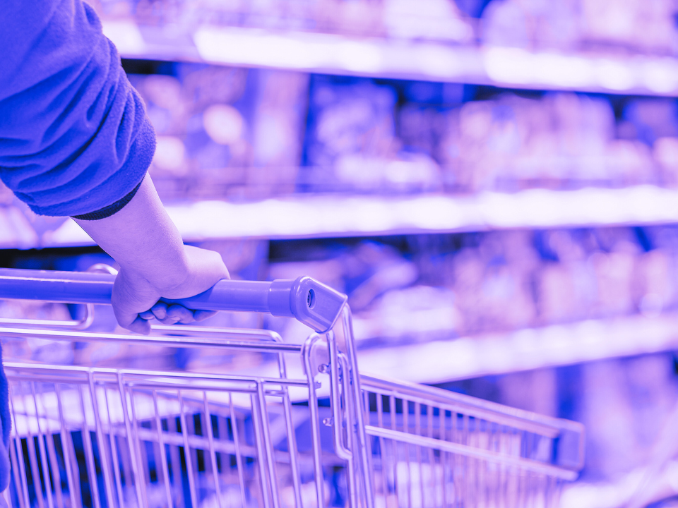 Purple-tinted image of a person pushing a shopping cart in a supermarket aisle, shelves stocked.