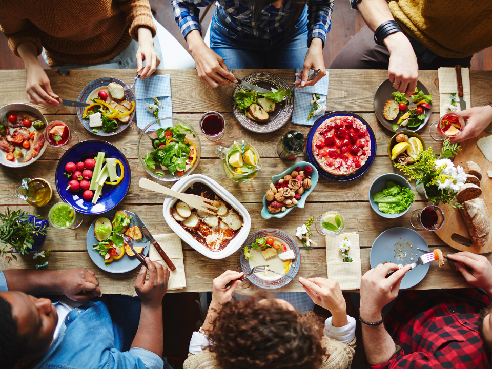 Top-down view of colorful dishes on a table with people dining together, used in an article: More Consumers Are Dining Out Again.