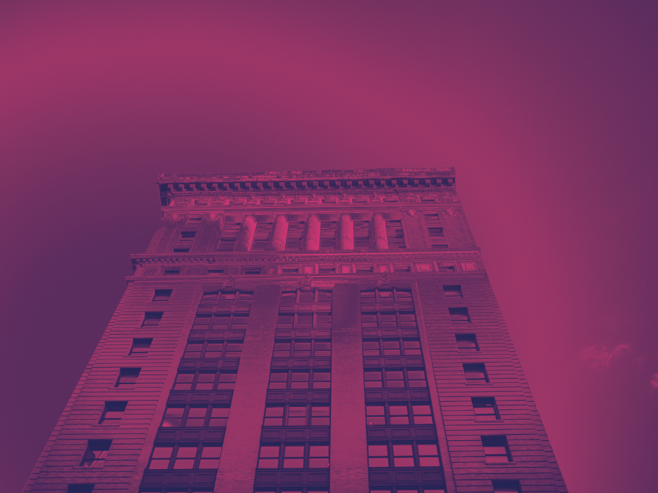 Tall brick building with ornate details, viewed from below against a clear sky, with a strong magenta overlay. For real estate article.