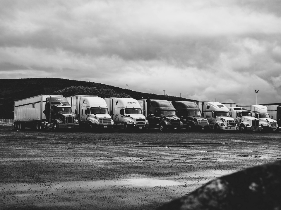 Row of parked semi-trucks in a wet lot under an overcast sky, with hills in the background. For real estate article: Triten and TPG.