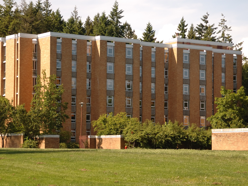 Brick building with rows of windows, surrounded by trees and greenery, under a partly cloudy sky. For real estate website article.