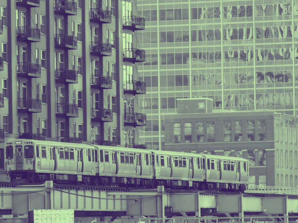 Elevated train in a city with an apartment on the left and modern glass building on the right. For real estate article: Miami & Suburban Chicago Rental Market.