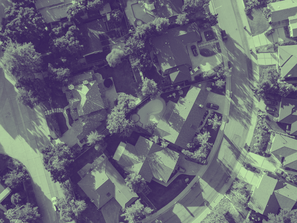 Aerial view of suburban homes, trees, a central pool, and winding road. Greenish tint; for real estate article on affordable southern cities.