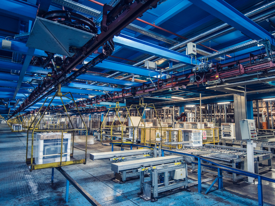 Modern industrial facility with blue beams, automated machinery, conveyors, rail lines, and metal platforms.