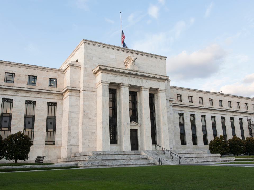 Neoclassical building with columns and half-staff American flag. Green lawn and trees. For real estate article on sales surge.