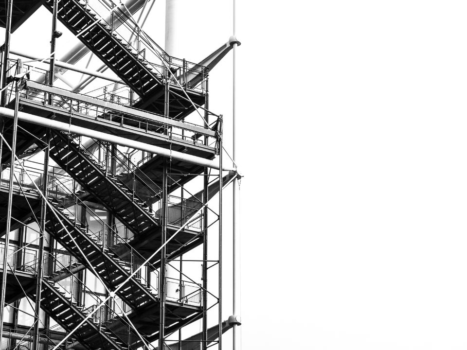 Black and white image of a metal scaffolding structure, featuring staircases and platforms. Featured in an article titled "Industrial Construction Costs Down.