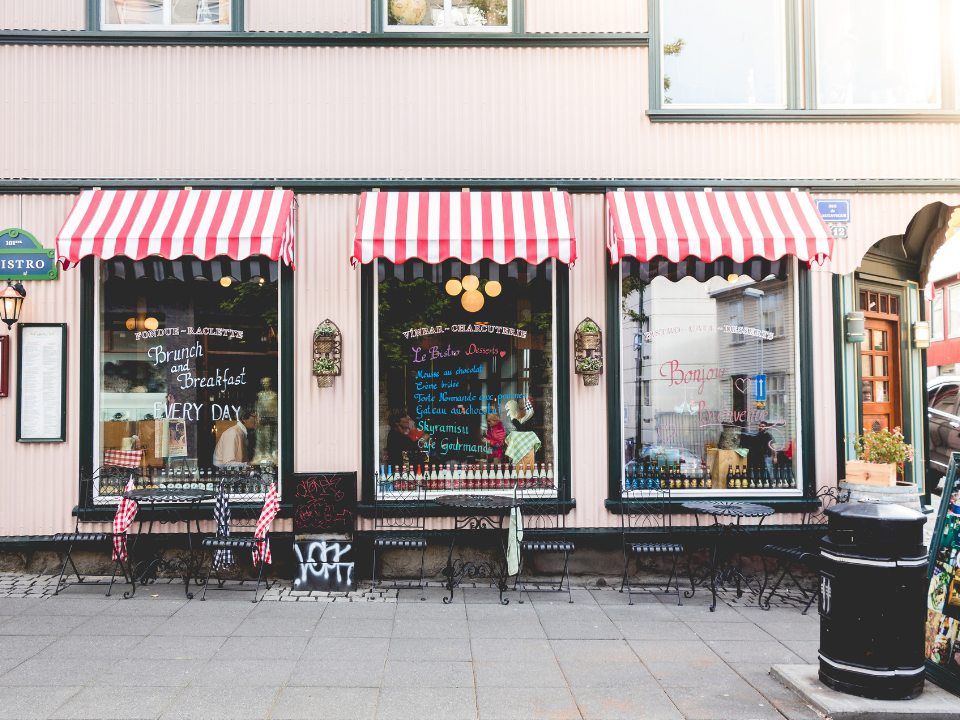 Charming café with striped awnings, outdoor seating, pink facade, and menu displays; featured in a real estate article.