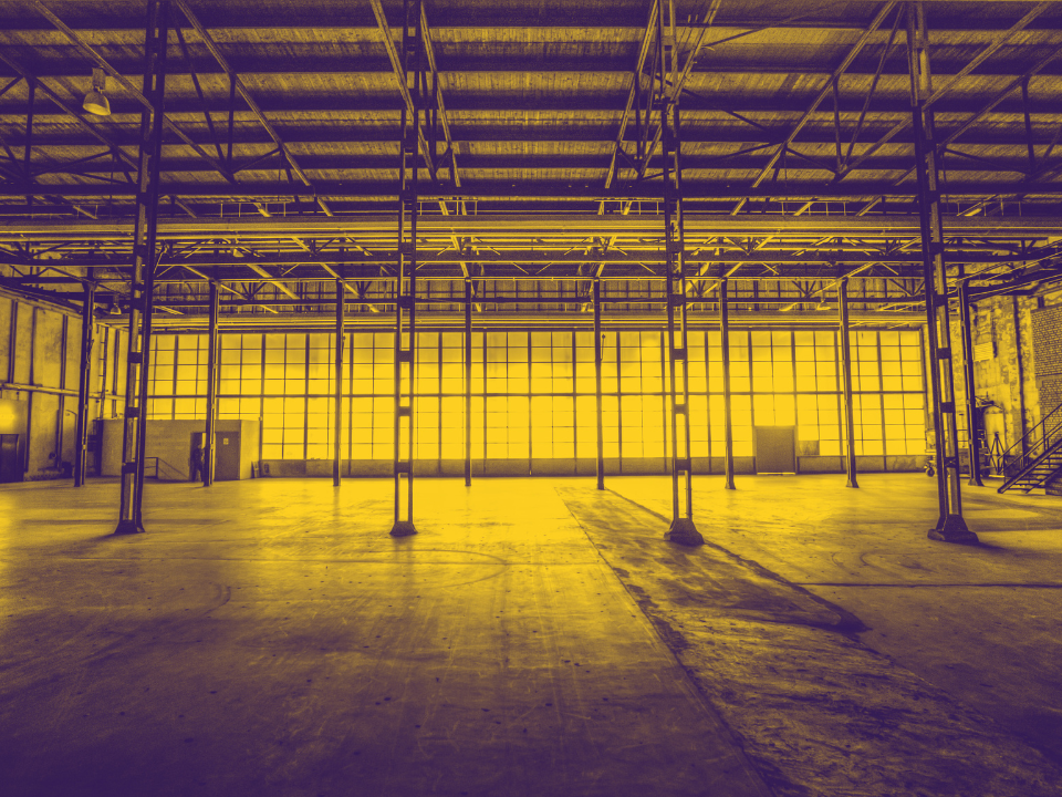 Empty warehouse with high steel-beam ceiling and large grid-patterned windows letting in warm light; featured on real estate site.