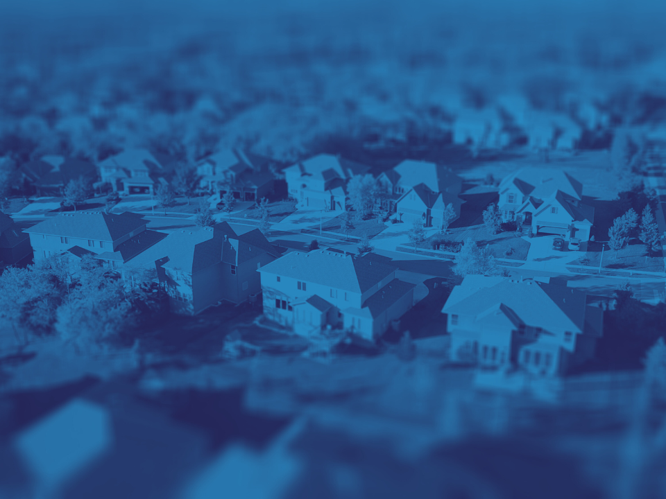 Blue-tinted aerial view of suburban houses with green trees and lawns, for a real estate article titled "What 2024 Has Taught CRE Pros.