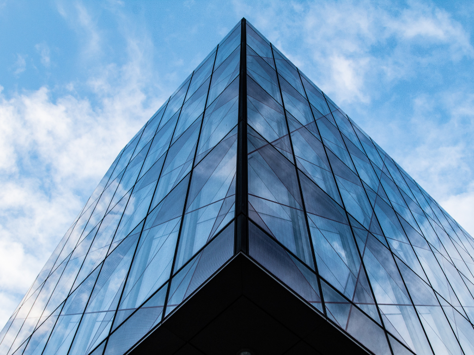 Modern glass building with triangular corner and geometric patterns against a cloudy sky, for real estate article on CRE.