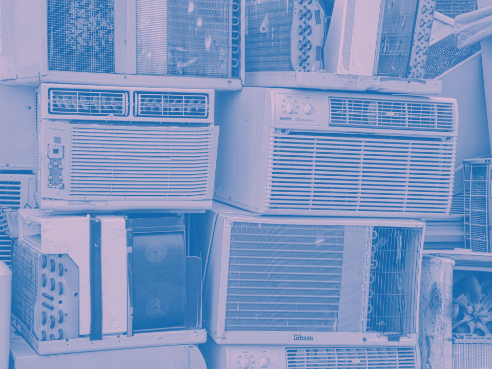 Stack of old window AC units in blue monochrome, diverse in size and design, for a real estate article on NYC AC mandate.