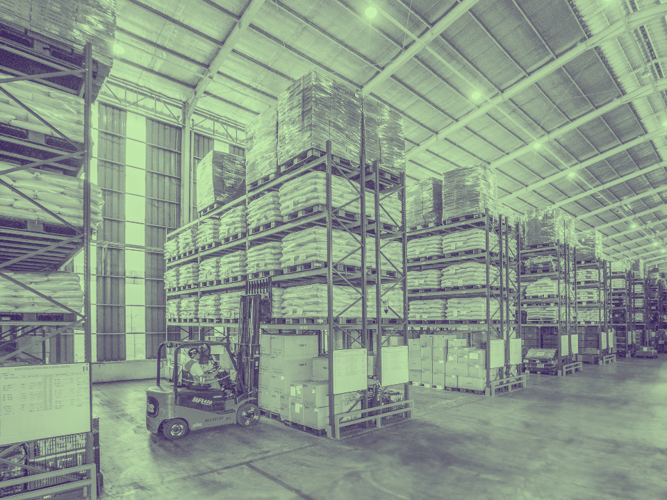 Warehouse interior with tall shelves of boxes. A forklift moves down the aisle, under blue-green tinted lights.