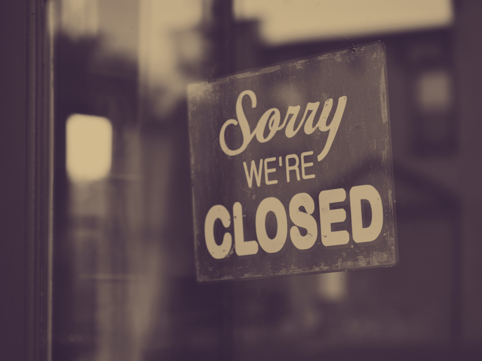 Sepia-toned image of a glass door with a weathered "Sorry, we're closed" sign, used in an article on distressed real estate.