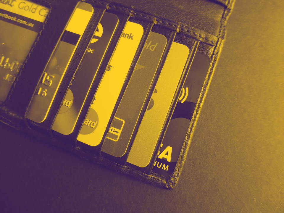 Wallet with six credit/debit cards, various designs and contactless symbols, with a yellow filter; for a real estate site article.