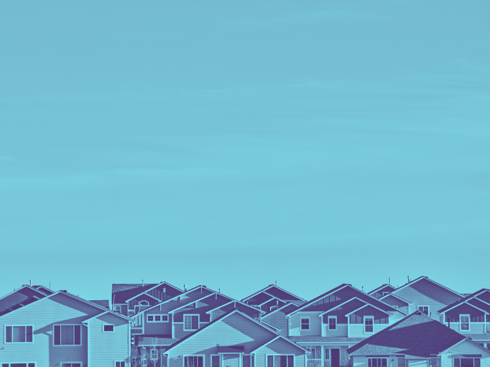 Suburban houses with gabled roofs under a blue sky, shown in monochrome. Featured in "U.S. Home Sales Plummet" article.