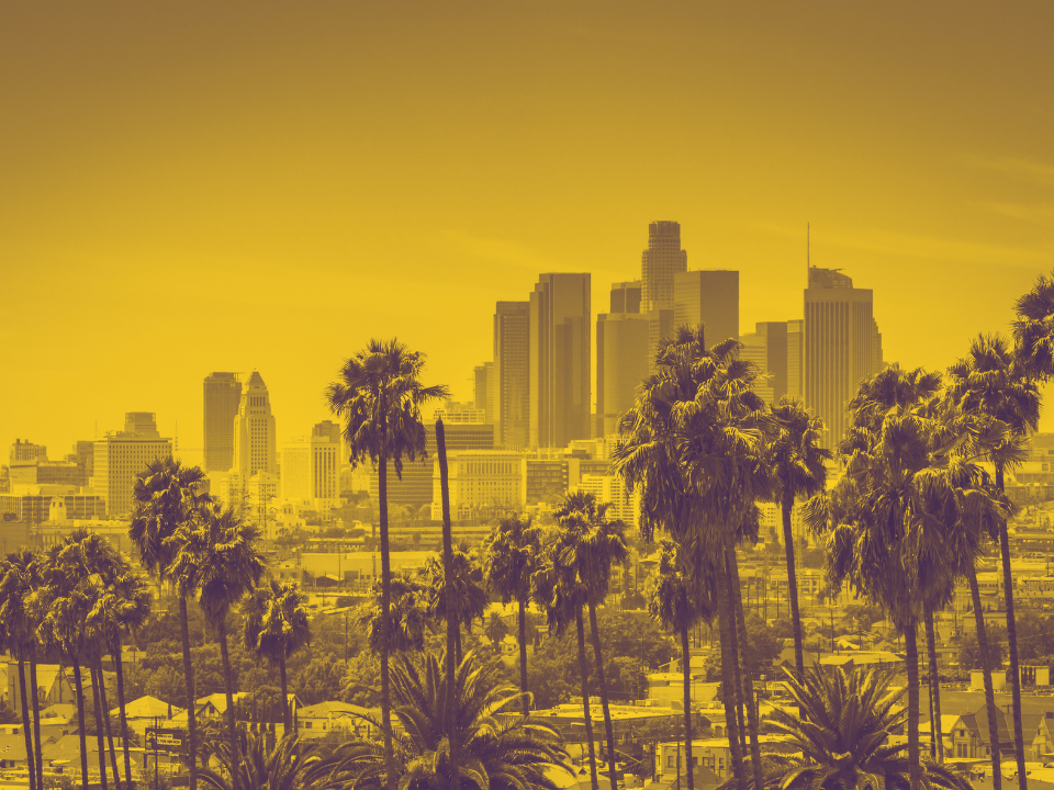 City skyline with tall buildings under a yellow filter, viewed through palm trees. Featured in real estate article on LA Mall refi.