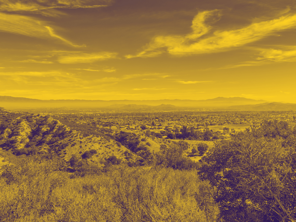 Scenic landscape: rolling hills, shrubs, cloudy sky. Distant city by mountains in golden tint. For real estate article on industrial leases.